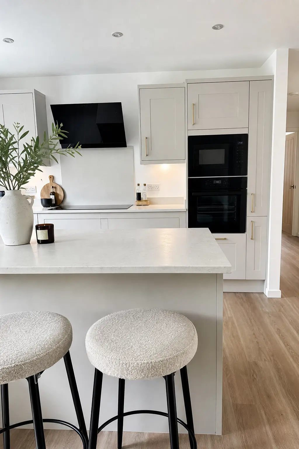 Pale grey shaker kitchen with a breakfast bar, built-in black ovens and boucle stools