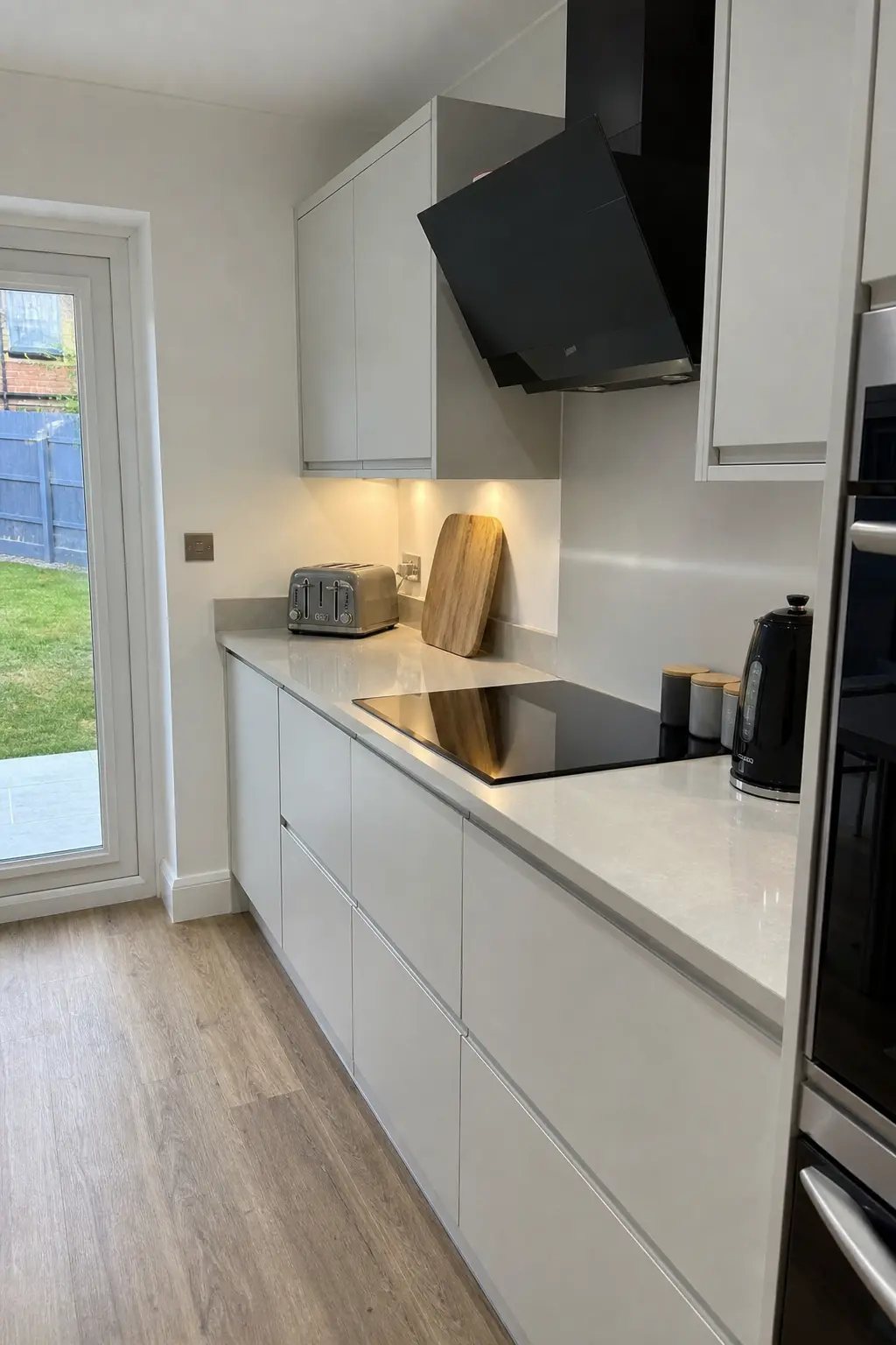 Light grey handleless galley kitchen with an induction hob and angled black extractor
